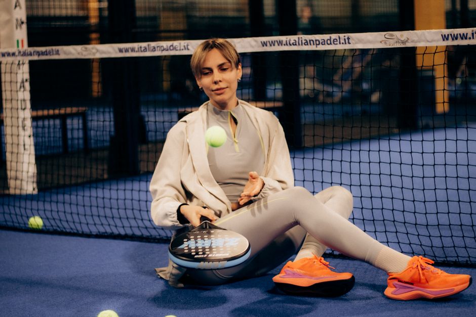 Een vrouw in sportieve padelkleding die speelt op de padelbaan, met een padelracket en bal.